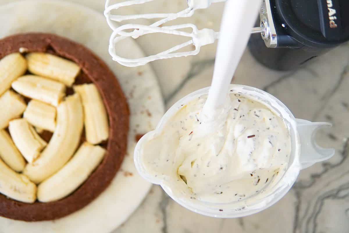 bottom of cake covered in bananas and a pitcher of whipped cream