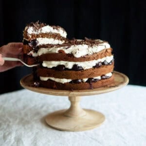 decorated Black Forest cake sitting on a wooden cake stand.