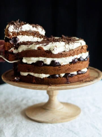 decorated Black Forest cake sitting on a wooden cake stand.