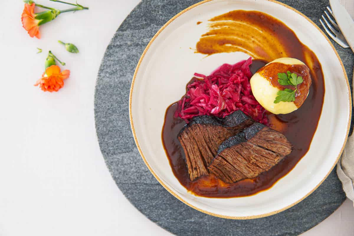 German beef pot roast on plate with potato dumplings and red cabbage