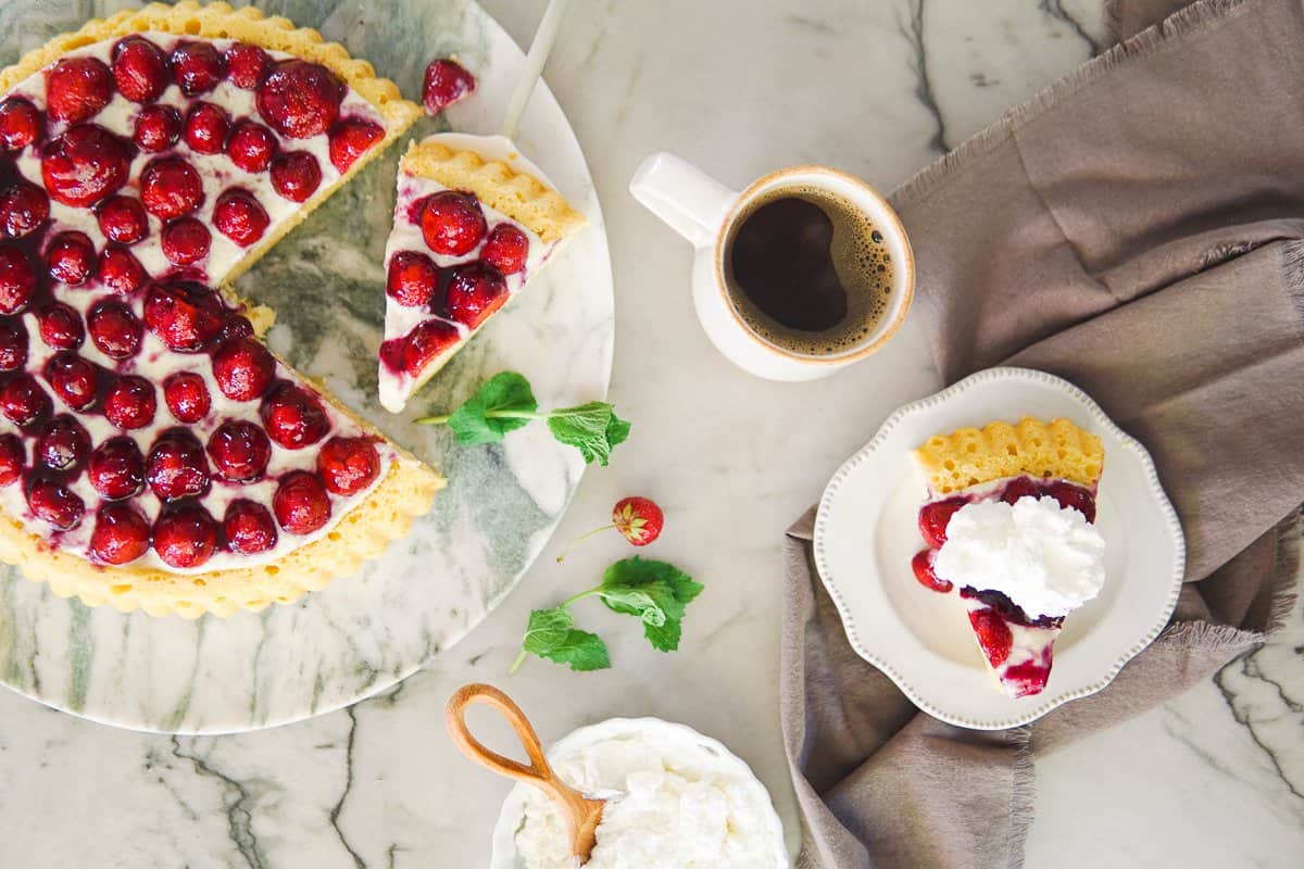 whole strawberry cake with cup of coffee and a slice of cake on a plate