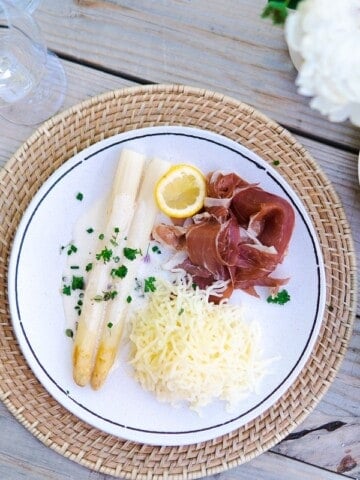 a plate with white asparagus, ham and potatoes, a cocktail and a bread basket