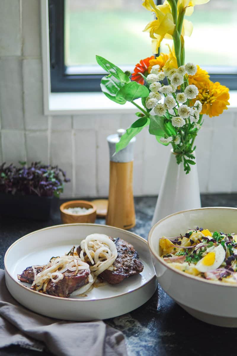 German grilled pork chops on a plate, potato salad in a bowl, and flowers