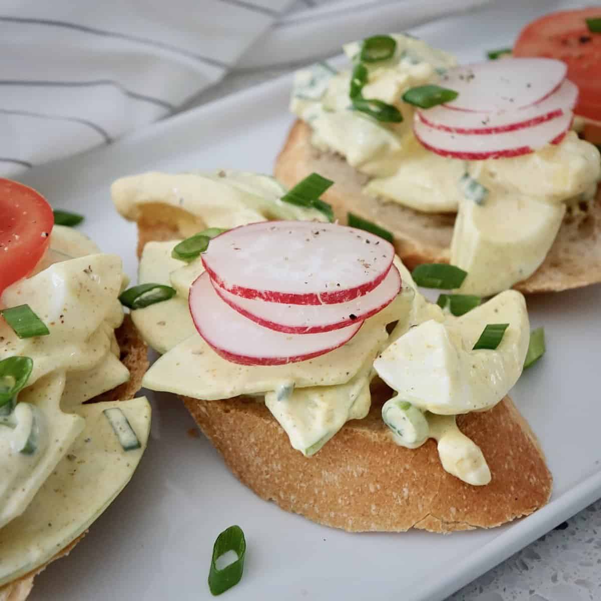 German curry egg salad served on baguette rounds with sliced radishes and sliced tomatoes