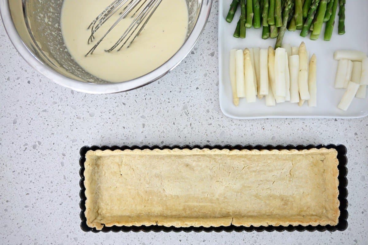 Bowl with quiche filling, plate with asparagus and quiche shell