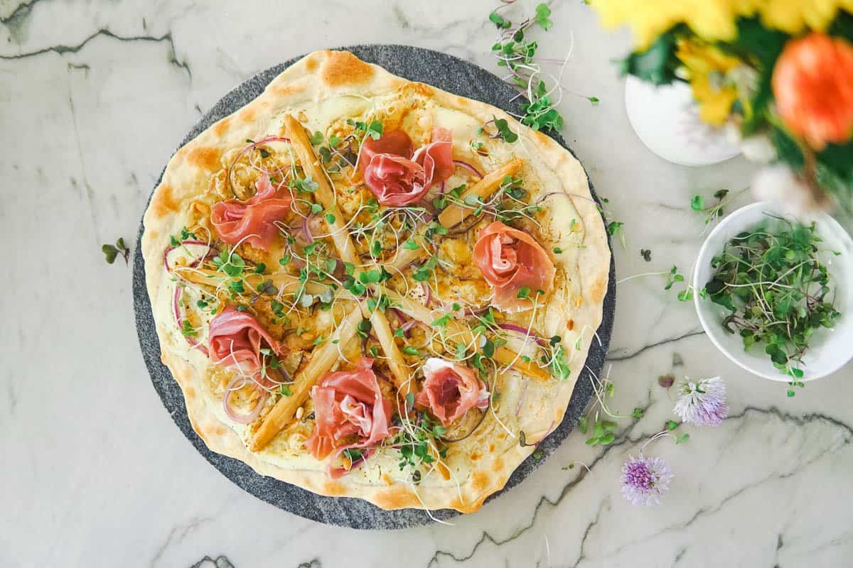 white asparagus flatbread on a stone platter with flowers on the side