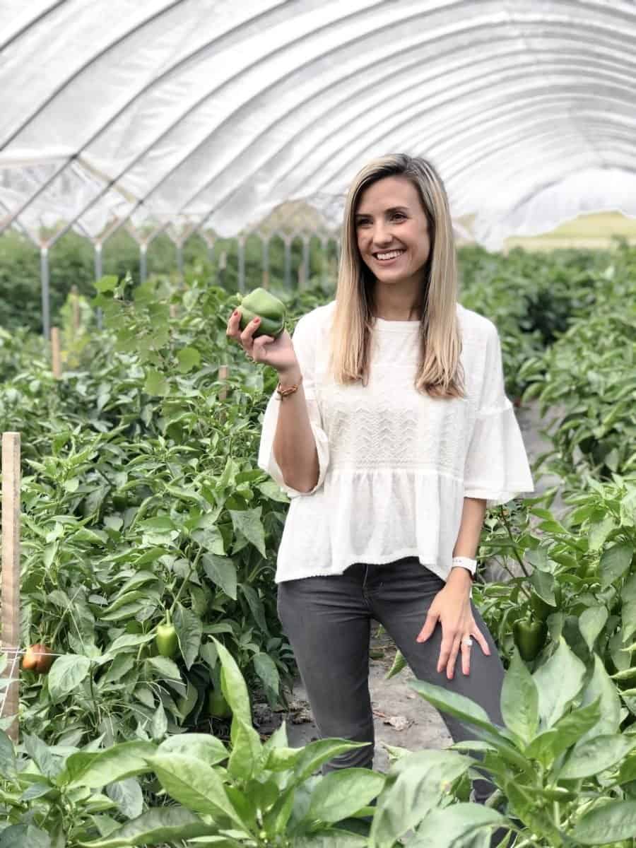 woman standing with bell pepper in hand in a greenhouse in Kansas