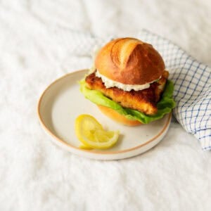 fried fish sandwich with remoulade sauce on a plate with a lemon.