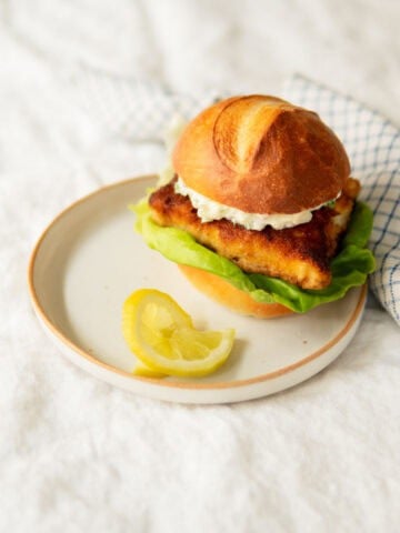 fried fish sandwich with remoulade sauce on a plate with a lemon.