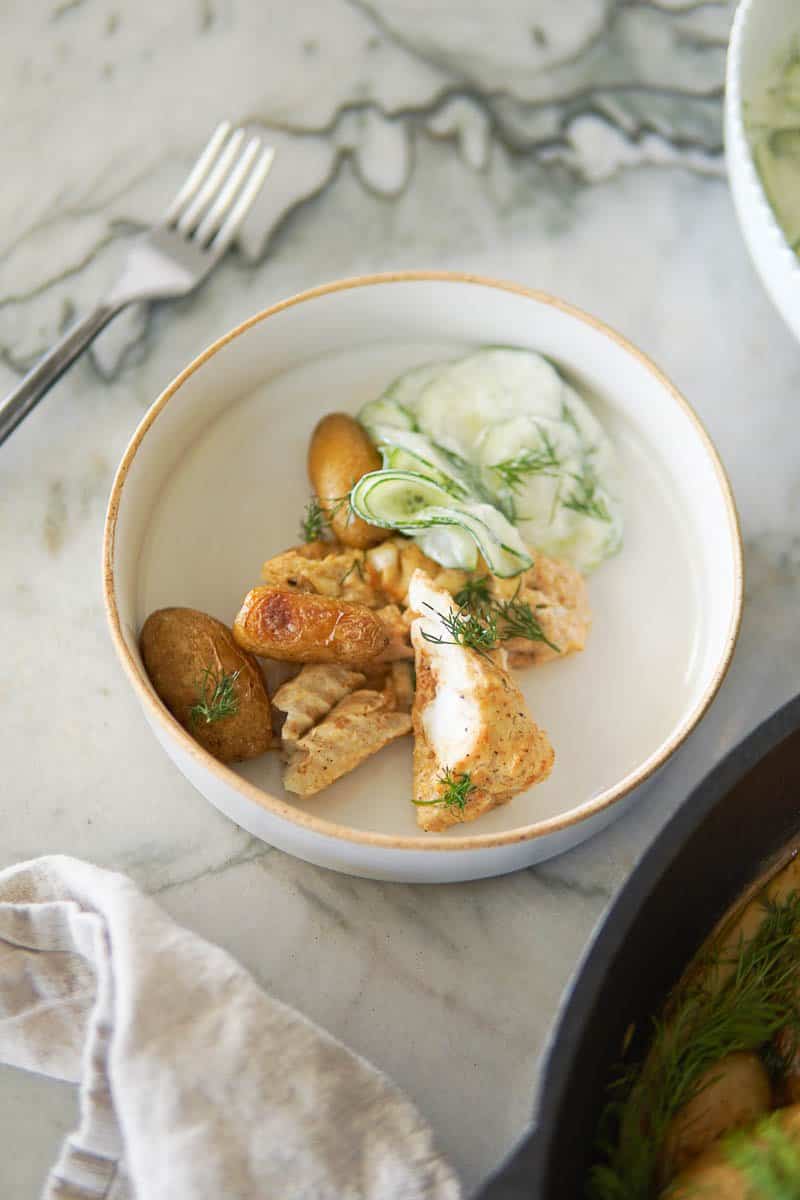 baked cod on a plate with potatoes and cucumber salad