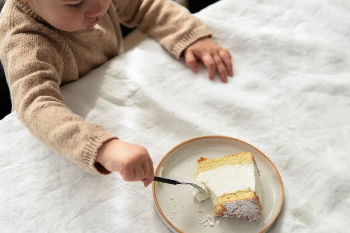 Ein kleines Kind isst ein Stück deutschen Käsekuchen mit einer Gabel.