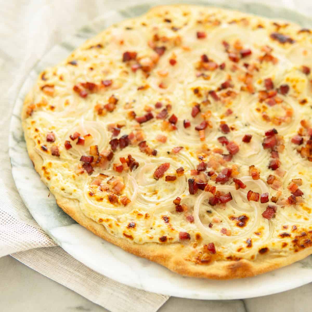 flammkuchen tarte flambee on a white marble plate