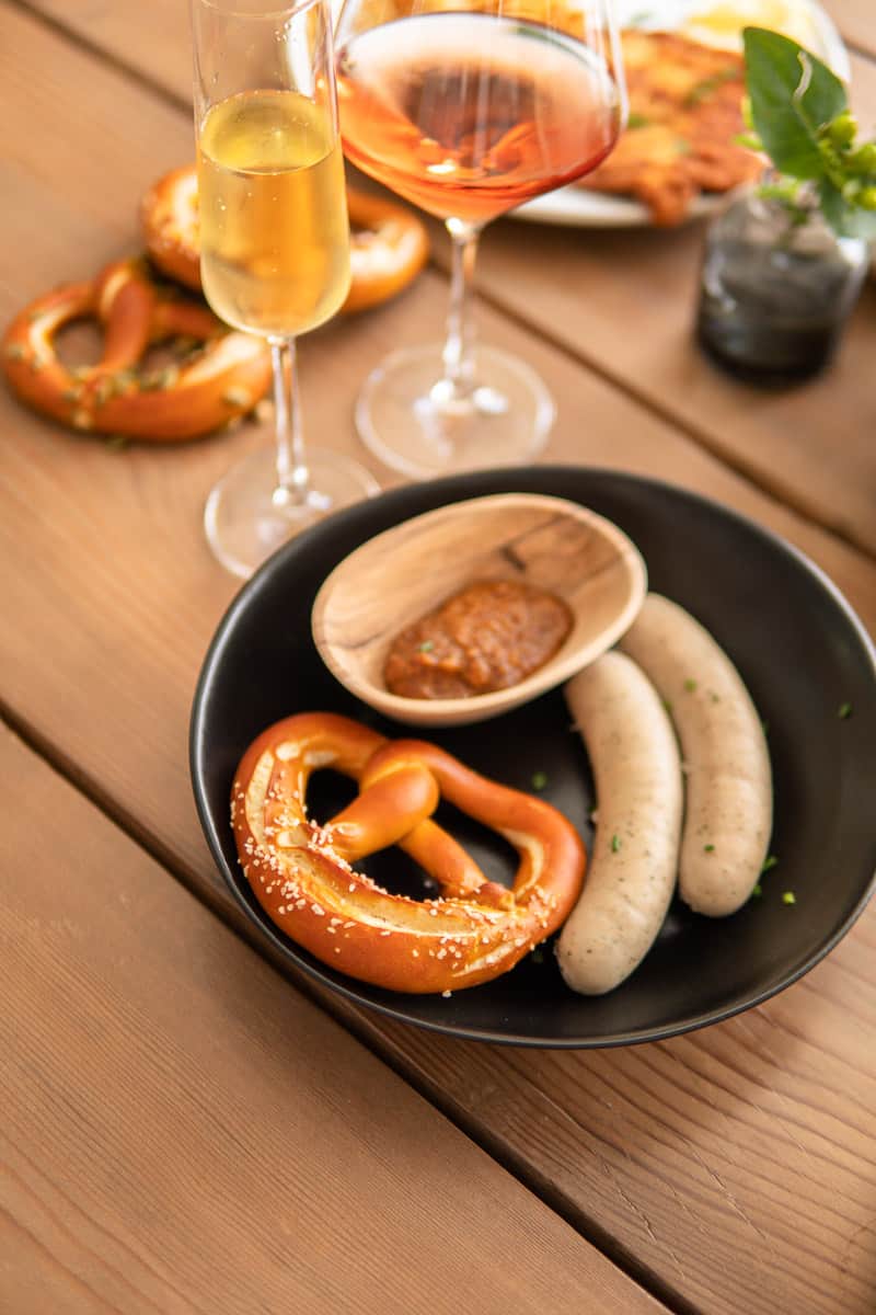 German sausage on plate with pretzels and glasses of wine next to the plate