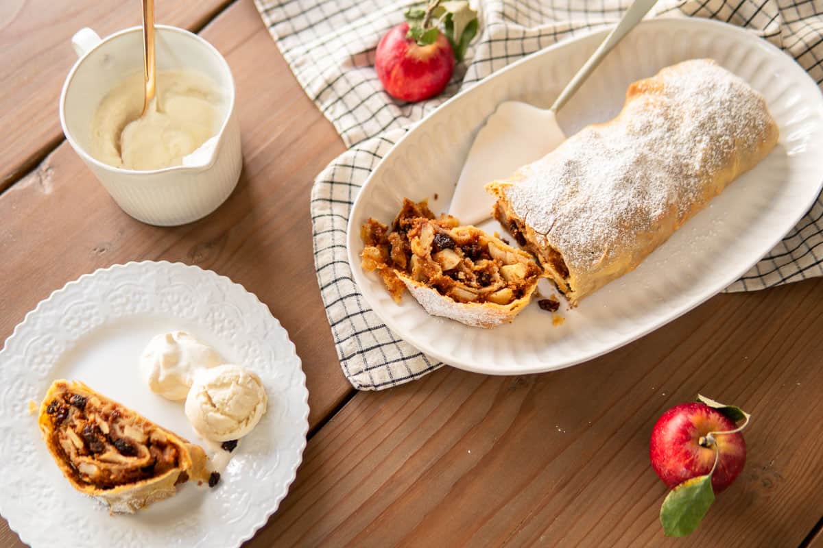 an apple strudel loaf on a platter and slices of apple strudel on plates