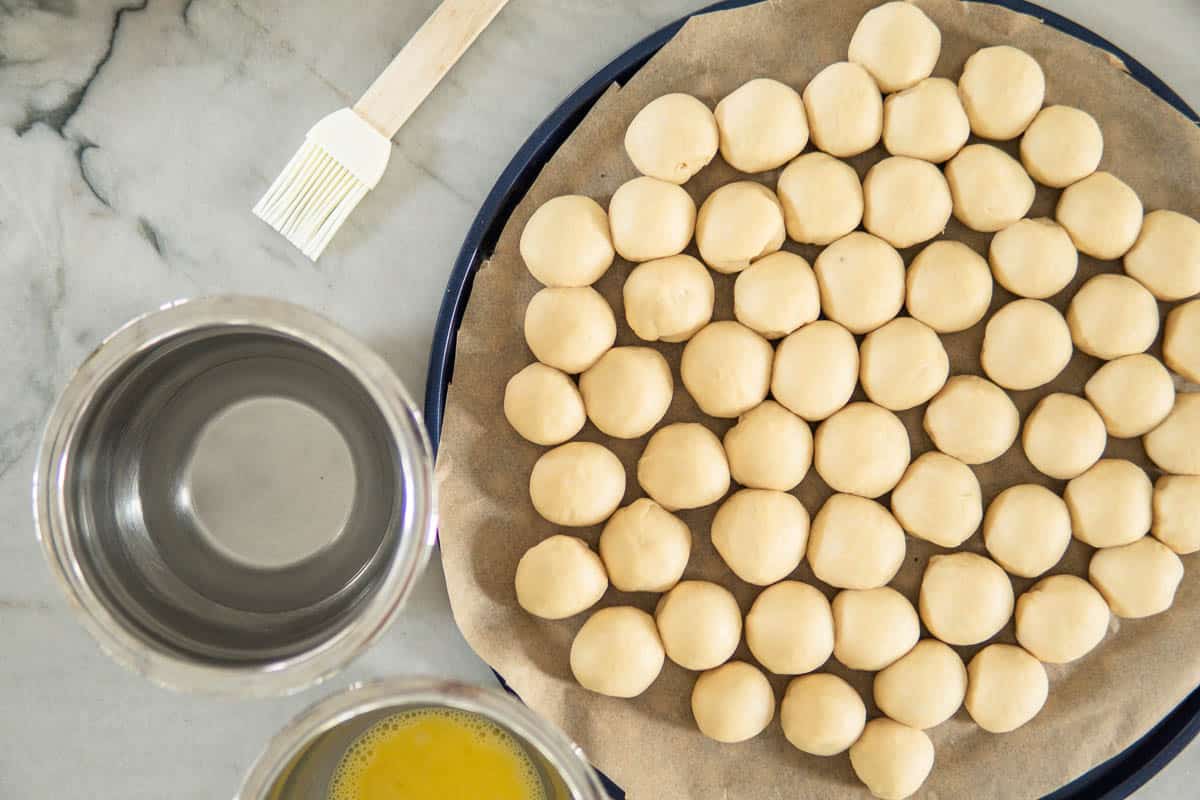 shaped balls nested together on a baking sheet with bowl of egg wash and lye solution next to it