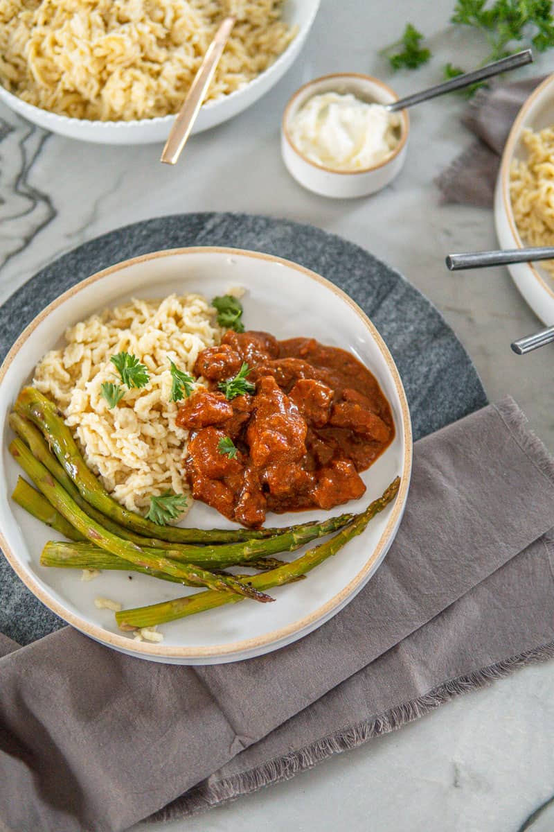 plate of German pork goulash with egg noodles and roasted asparagus