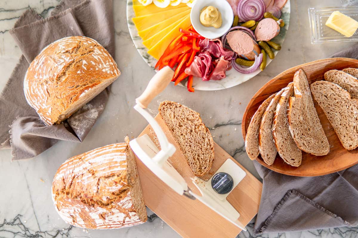 fresh baked sourdough bread next to bread slicer and a meat and cheese board