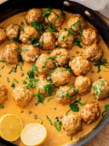 pan filled with German meatballs in sauce and garnished with parsley and lemon