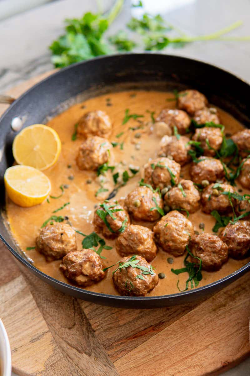 German meatballs in a creamy caper sauce garnished with fresh parsley and lemon halves