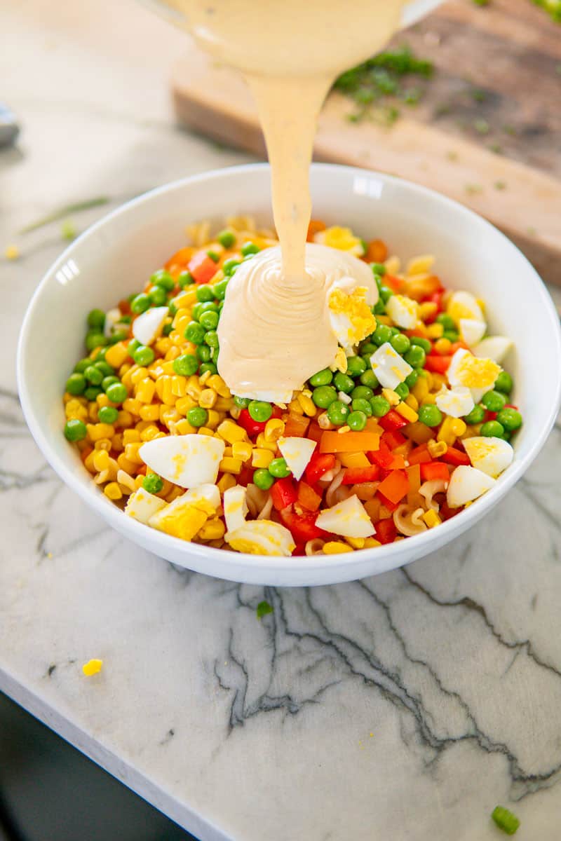 pouring creamy dressing over pasta salad