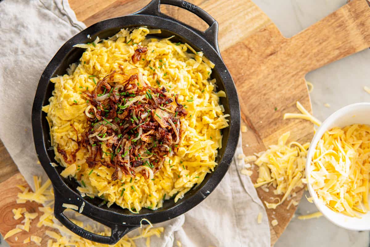 a cast iron dish filled with German cheese spätzle and topped with caramelized onions and chives