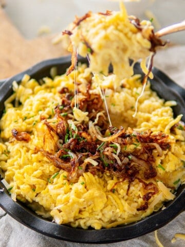a cast iron dish filled with kaesespaetzle and topped with caramelized onion and chives