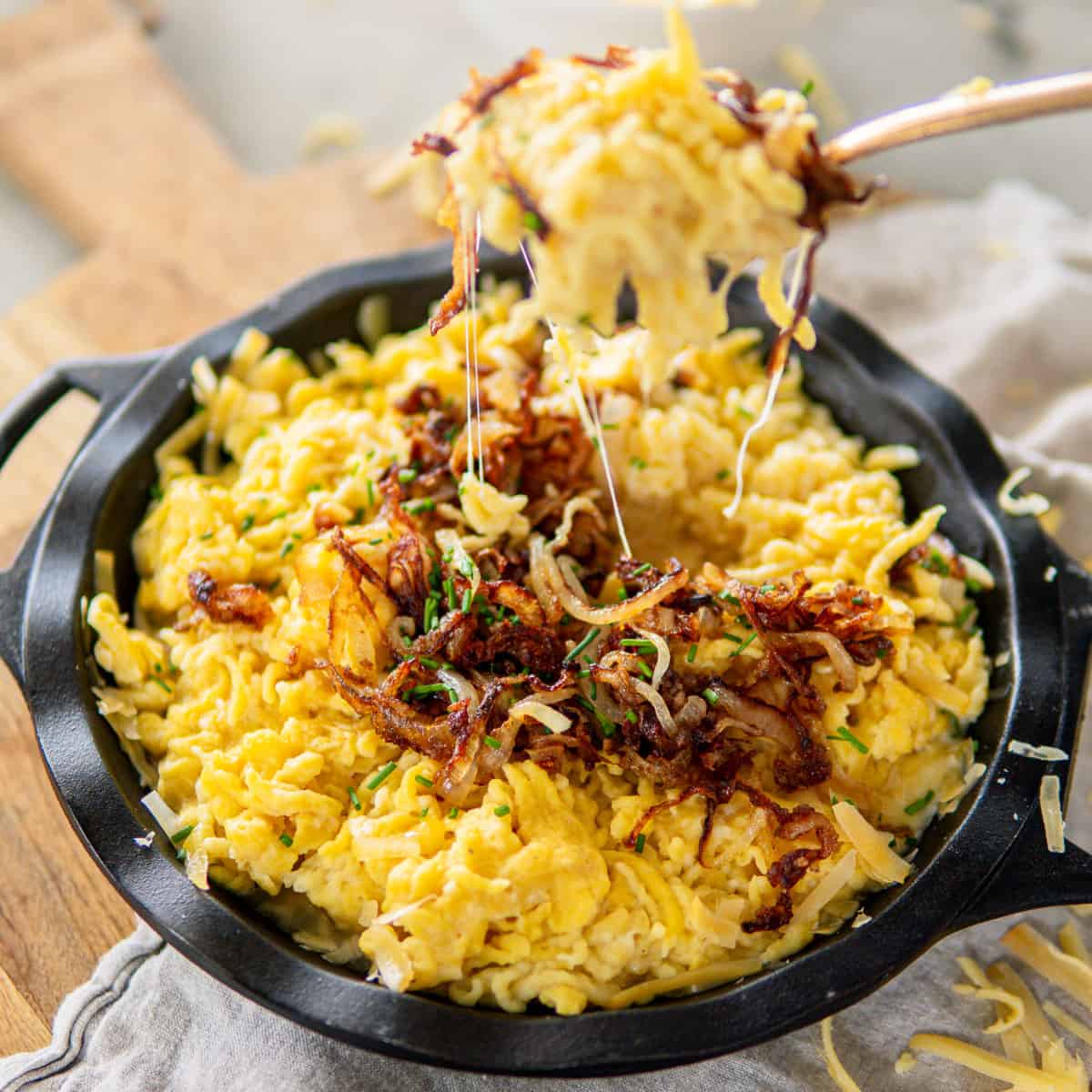 a cast iron dish filled with kaesespaetzle and topped with caramelized onion and chives