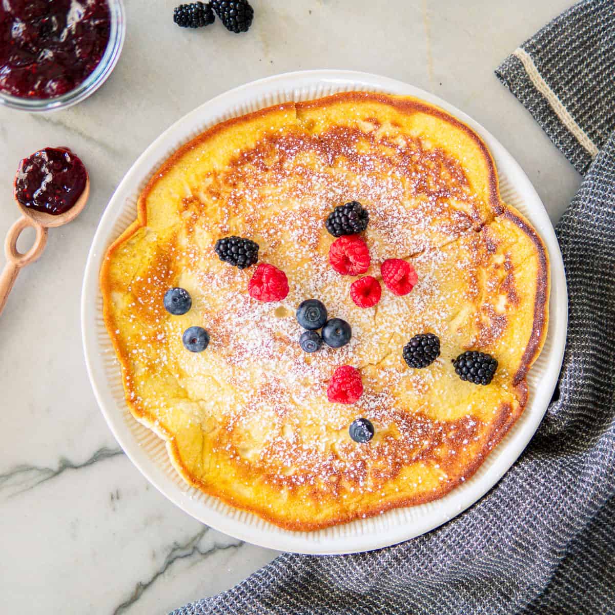 German pancake on a large plate topped with powdered sugar and berries