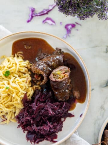 beef rouladen on a plate with noodles and red cabbage