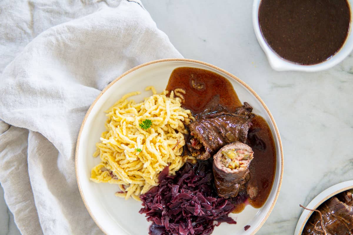 closeup of cooked beef rouladen cut in half, egg noodles and red cabbage