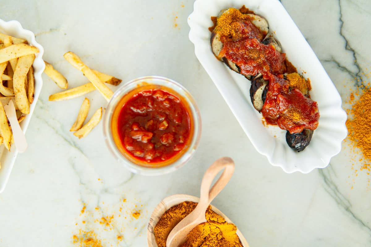 curry sauce in a glass jar surrounded by a sliced curry wurst and fries