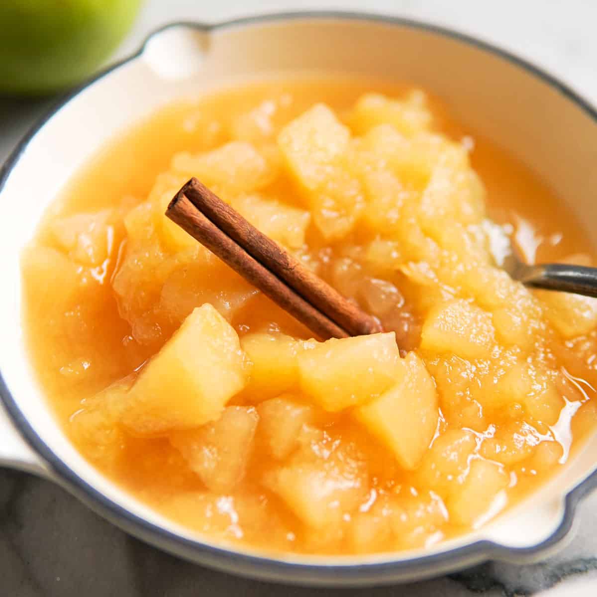 chunky apple sauce in a white dish with a cinnamon stick