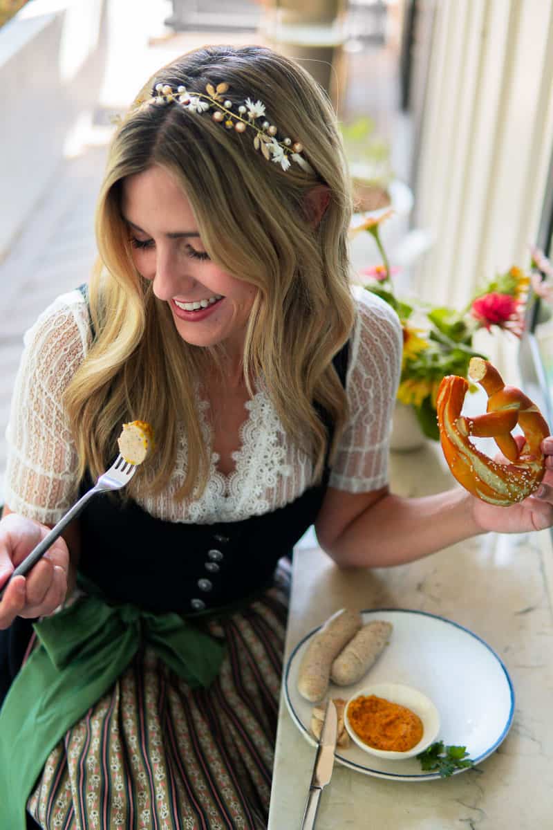 girl in a Bavarian dress eating Weisswurst and pretzel