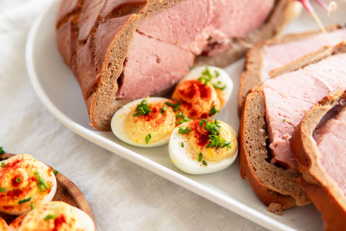 Deviled eggs sitting alongside some sliced, baked ham on a platter.