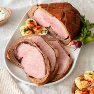 A baked ham wrapped in bread sliced open and served on a white platter.