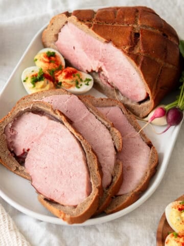 A baked ham wrapped in bread sliced open and served on a white platter.
