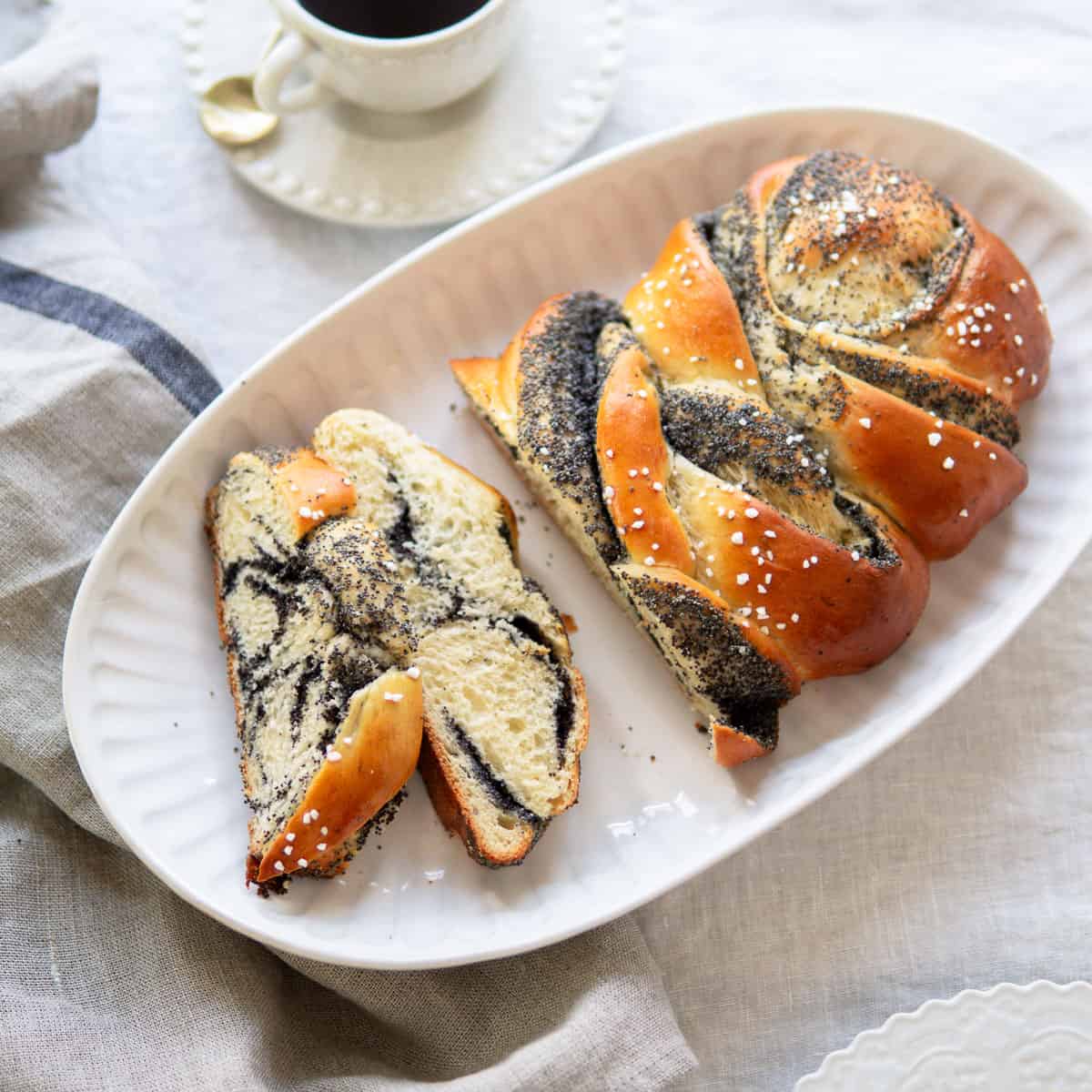Braided bread with poppy seed filling cut into slices and a cup of coffee.