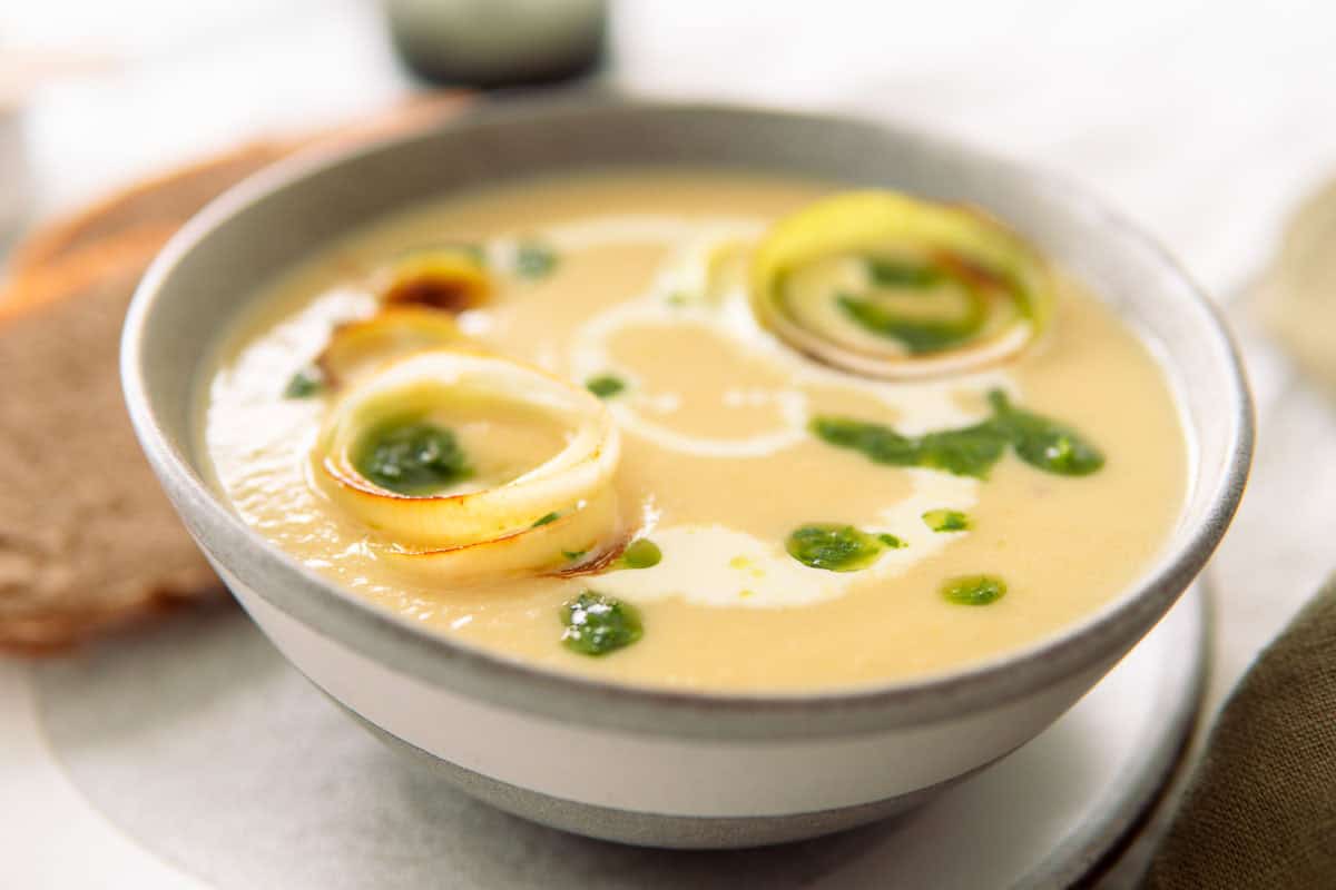 closeup of a bowl of creamy leek and potato soup garnished with cream, parsley oil and leeks