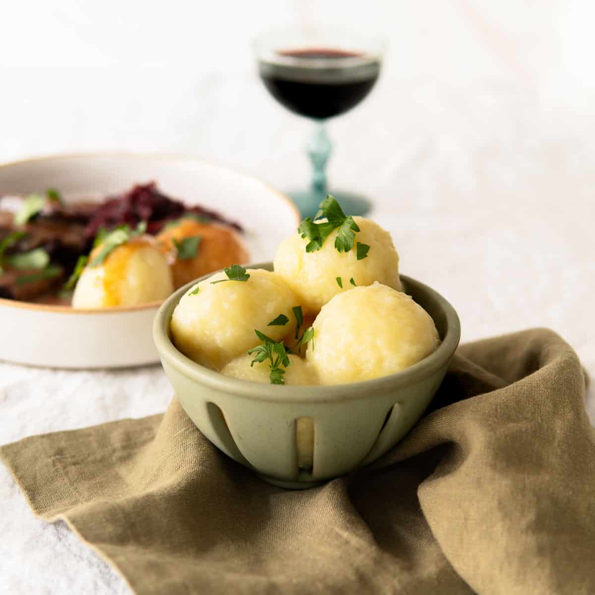 German potato dumplings in a bowl with parsley sprinkled over the top and in the background plated with a roast and red cabbage.