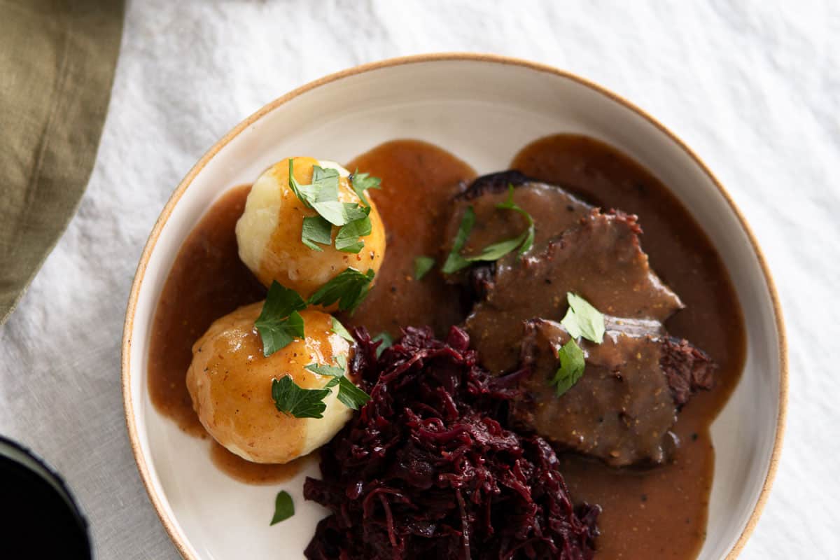 German potato dumplings on a plate with a German beef roast, sauce and red cabbage.