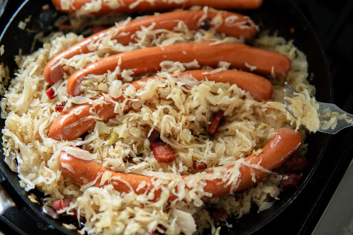 Sauerkraut heating in skillet with bacon bits and Wiener sausages by Schaller & Weber.