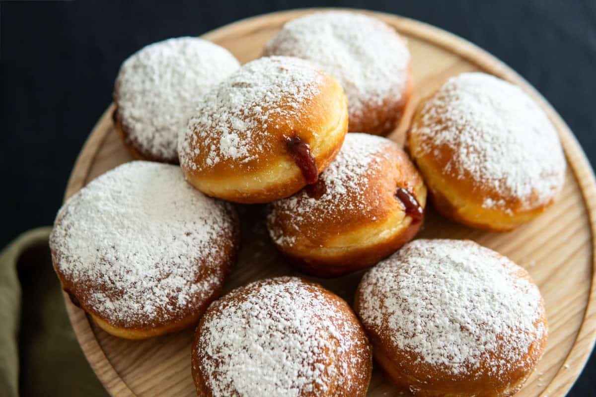 A pile of Berliner German donuts on a wooden platter.