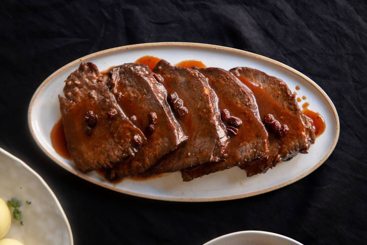 A platter with sliced Sauerbraten topped with silky dark sauce with raisins in it.