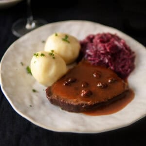 Sauerbraten slice on a plate with sauce, potato dumplings and red cabbage.