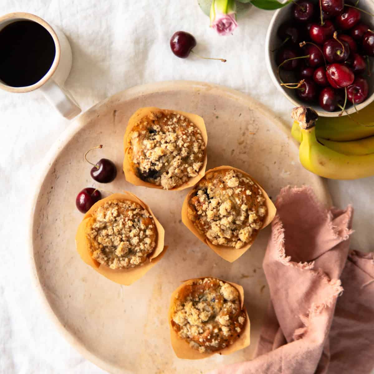 Banana muffins with cherries on a platter with a cup of coffee next to it.
