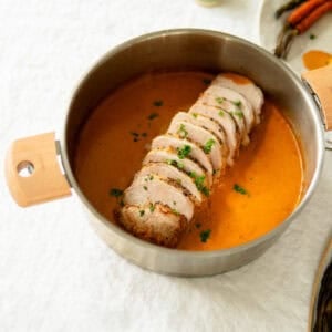 Pork loin roast sitting in sauce in a pan.