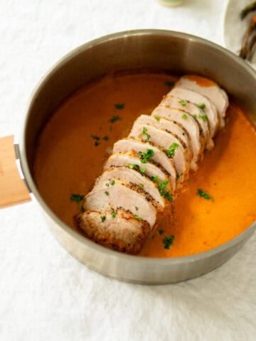 Pork loin roast sitting in sauce in a pan.