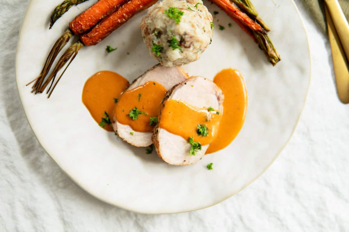 Close-up of German pork loin roast on a plate with an orange sauce poured over the top.