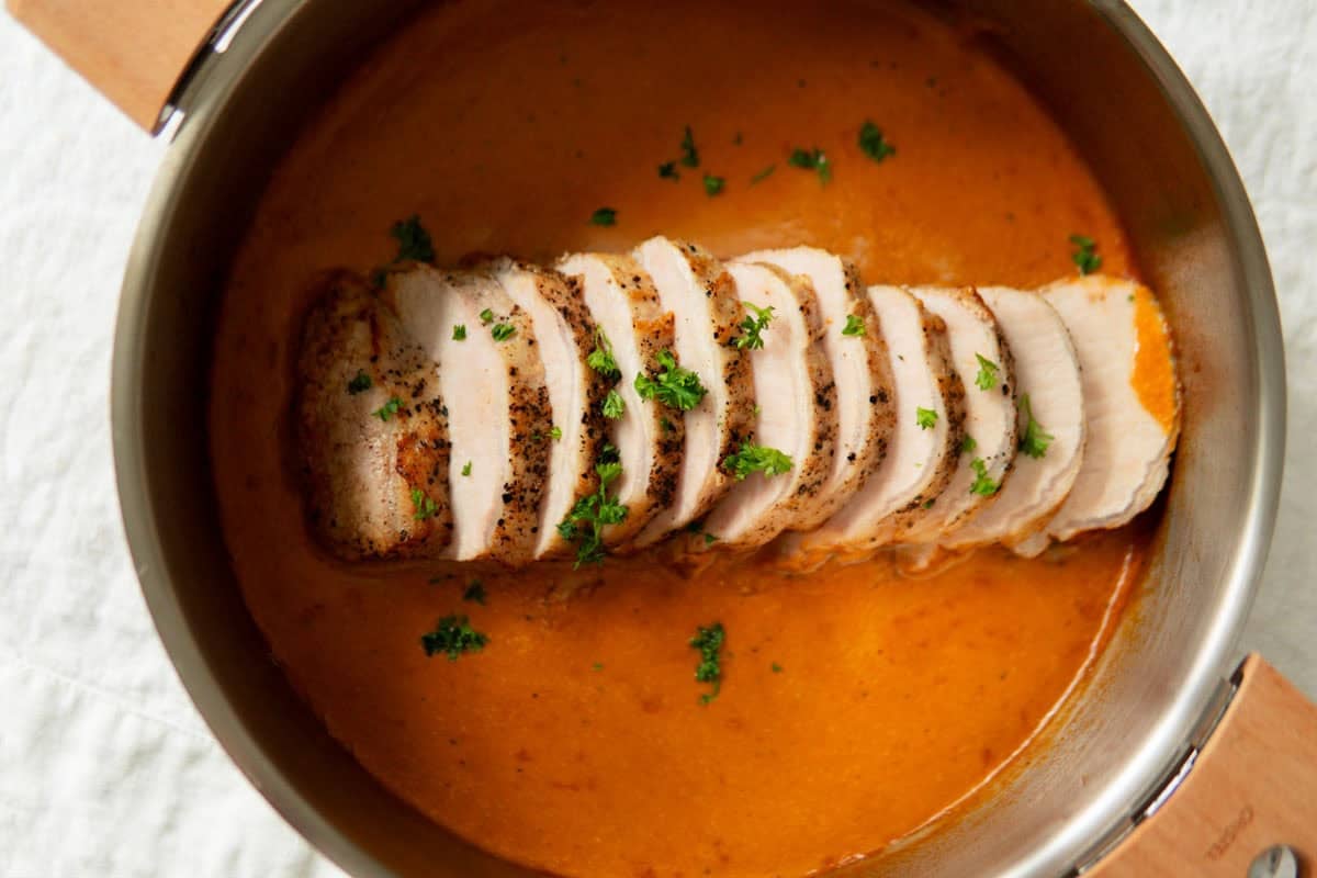 Closeup of sliced ​​German pork loin roast sitting in a pan with sauce.