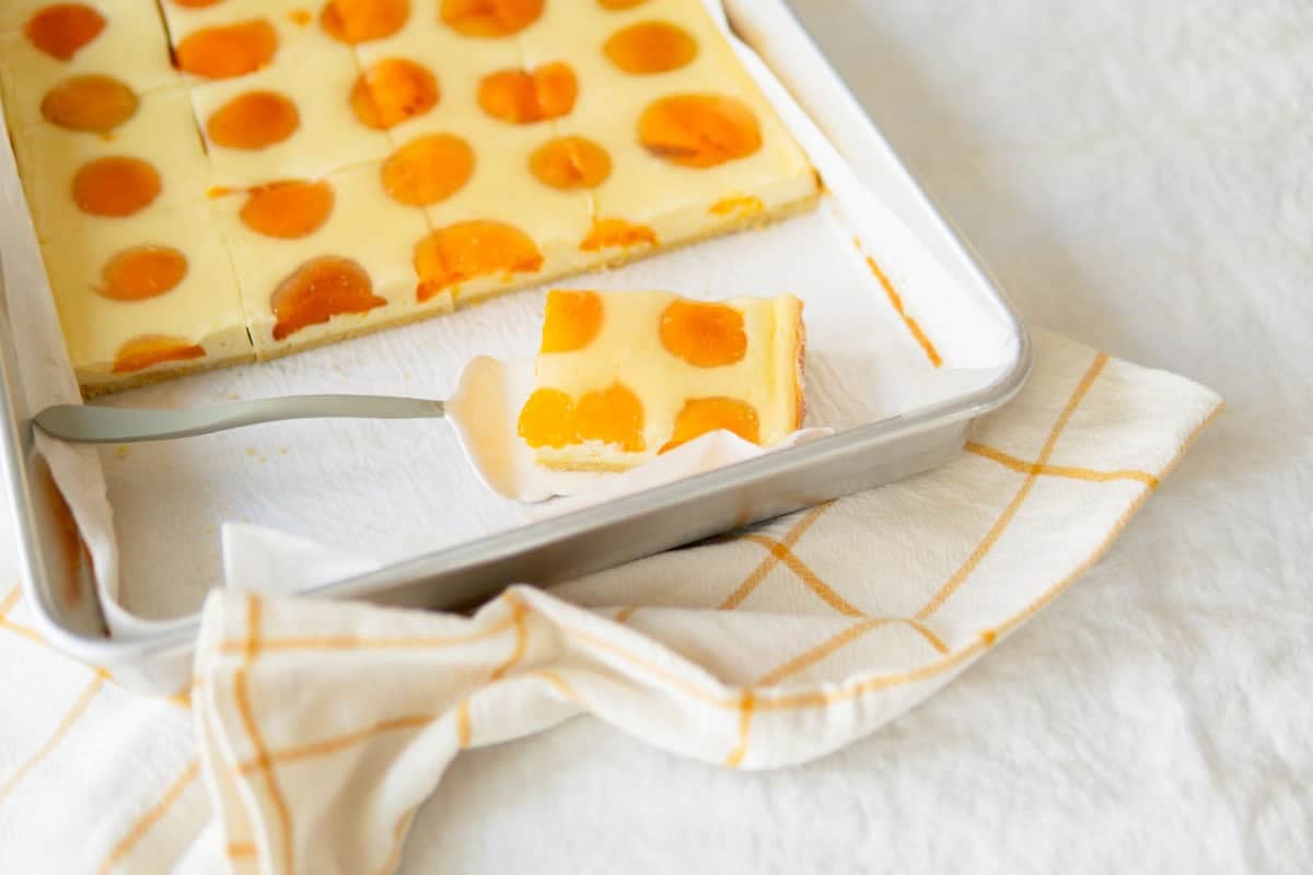 Apricot cake in a cake pan with one slice sitting on a cake server.